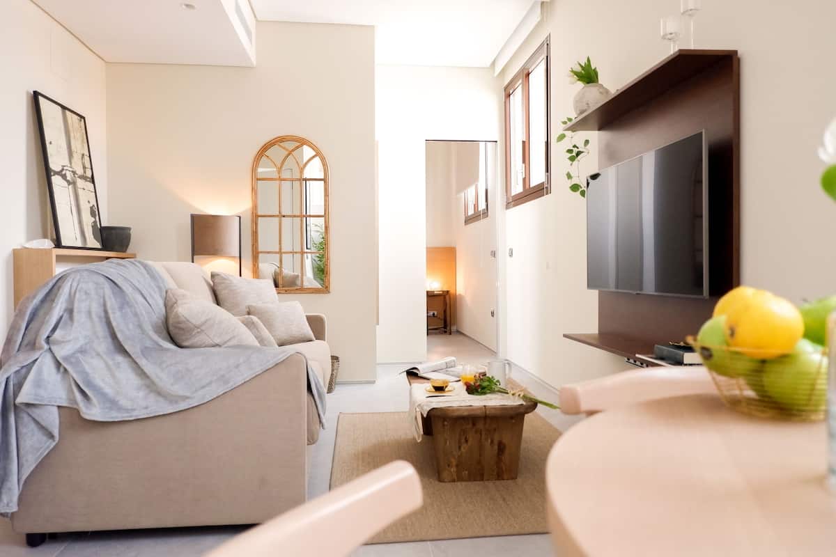 Una sala moderna con un sofá, una mesa de centro y un televisor. Se ve una ventana con vistas al exterior.