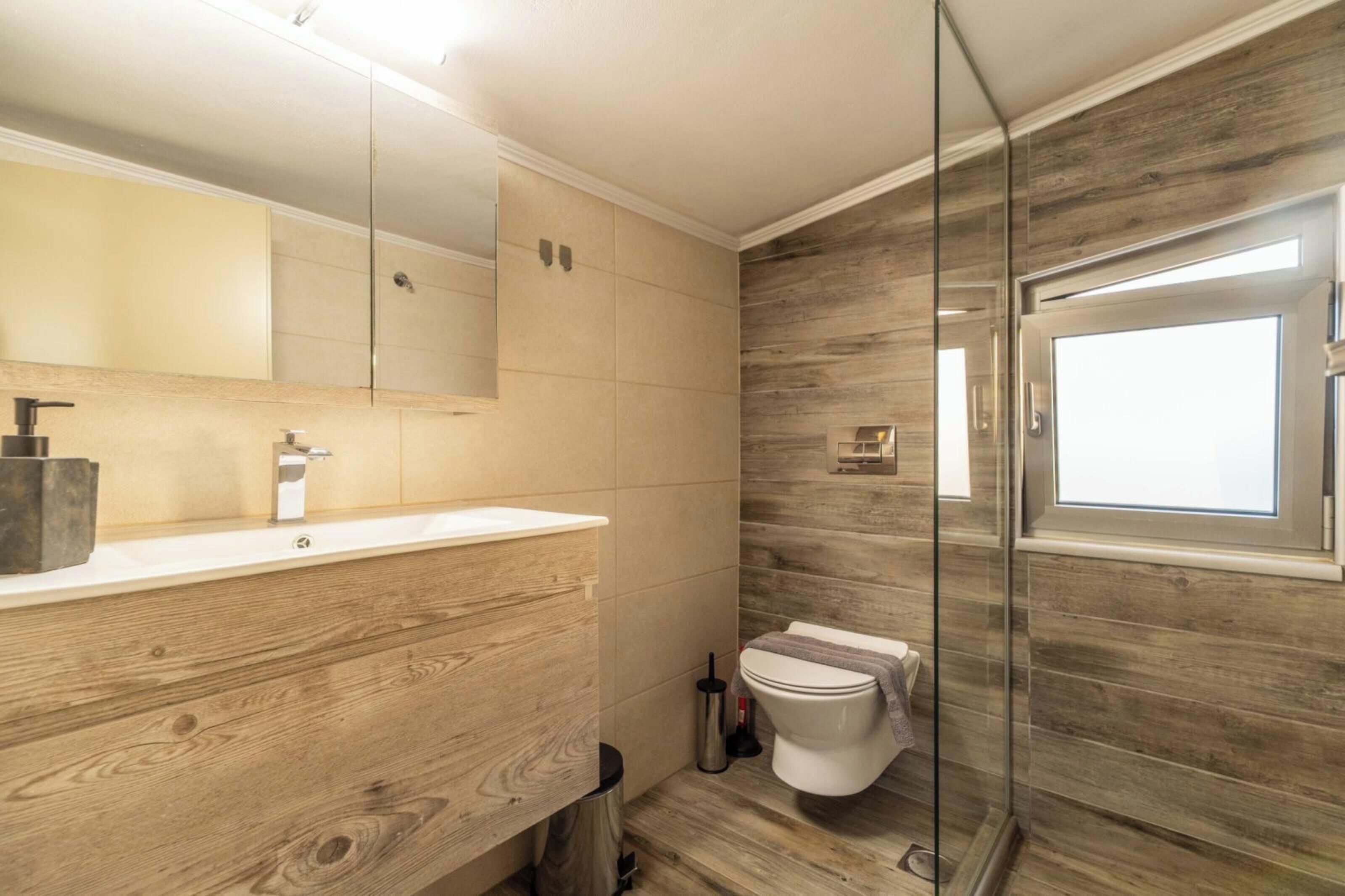 Ein modernes Badezimmer mit einem Holzkosmetikschrank, einer Duschkabine aus Glas und einer Toilette.