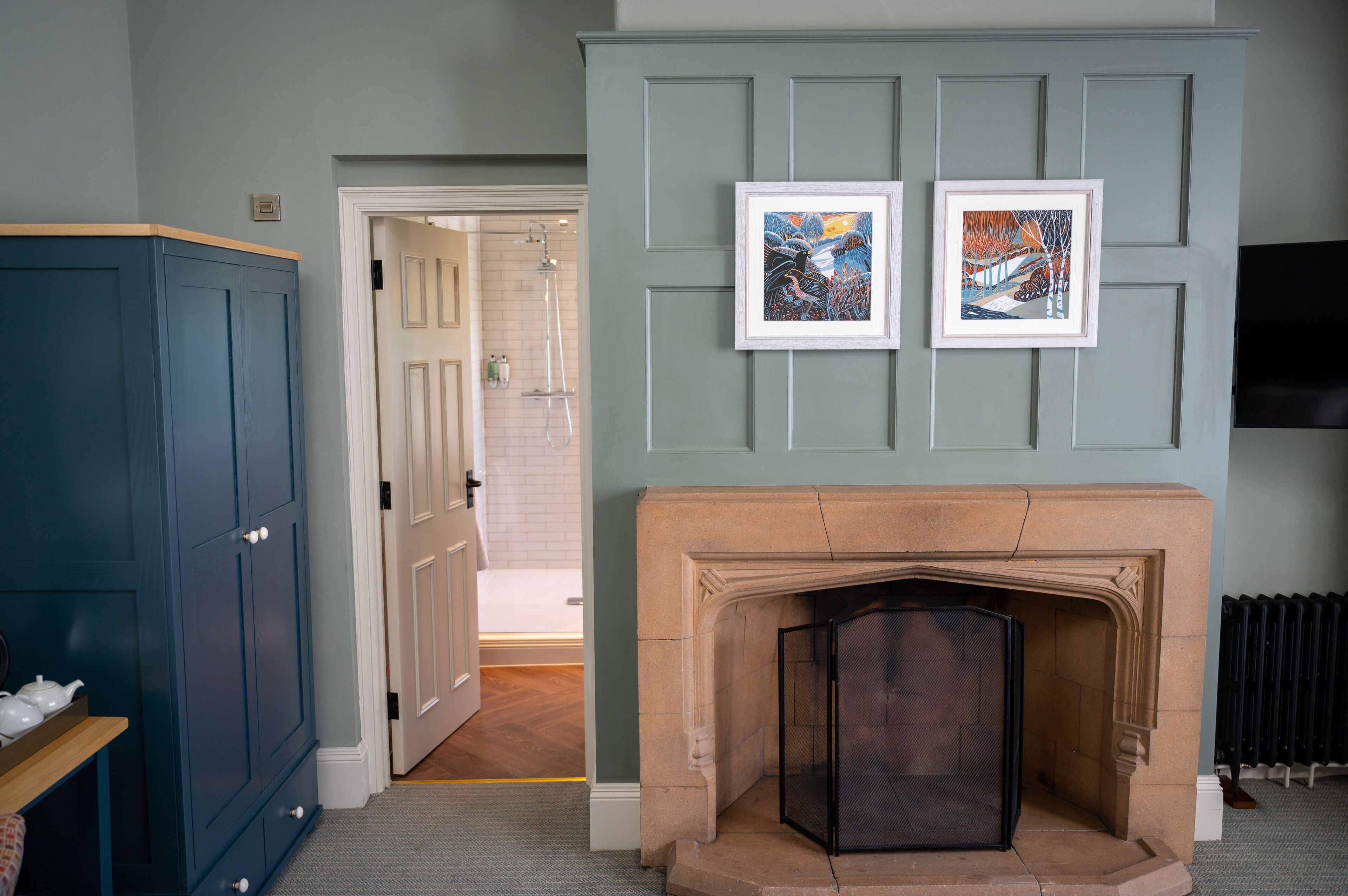 A room with a fireplace, two framed artworks, a television, and a wardrobe.