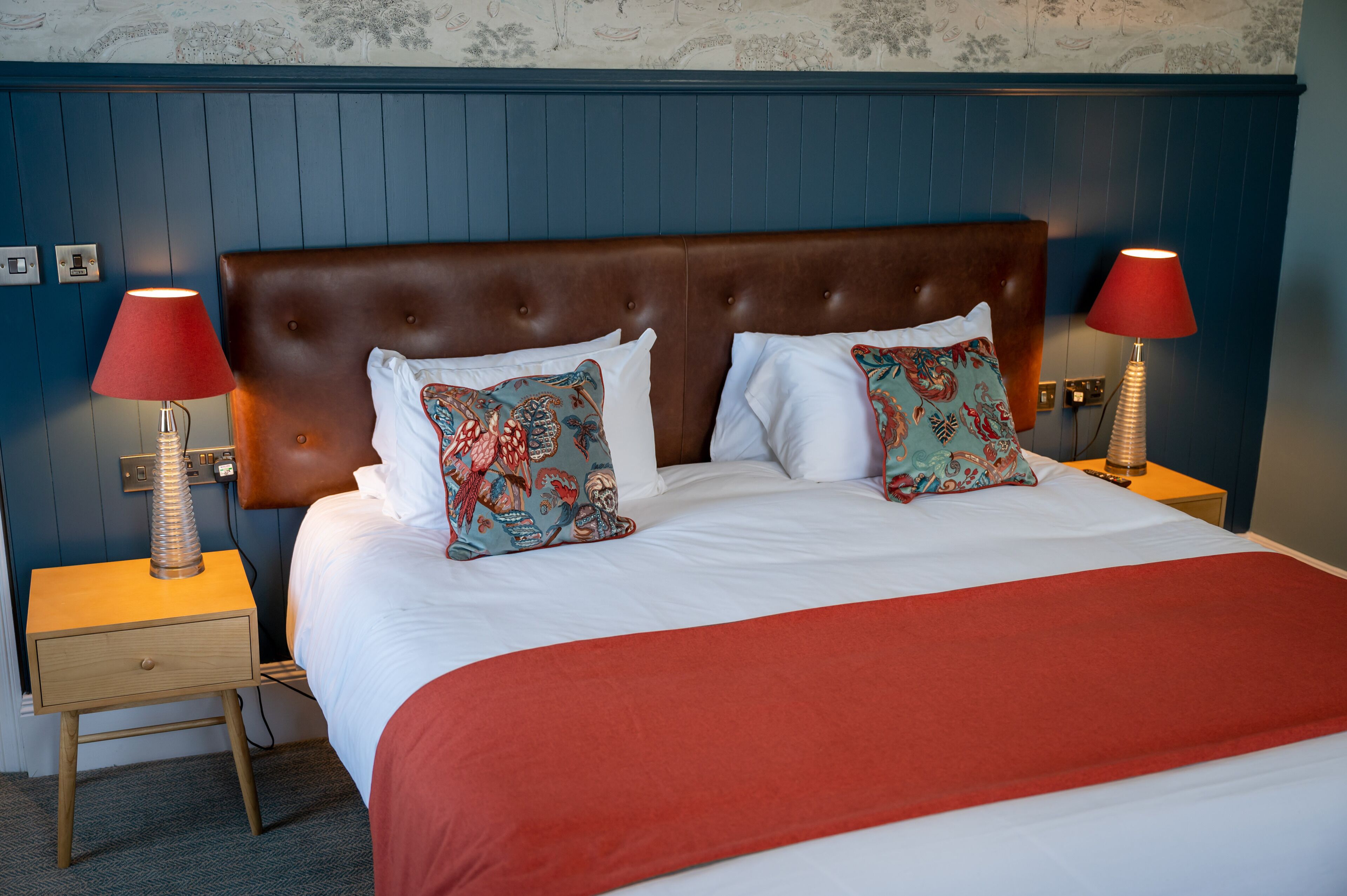 A neatly made bed with a brown headboard, two red lamps, and patterned pillows.