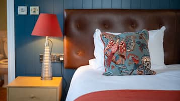 A neatly made bed with a patterned pillow, a red lamp on a wooden nightstand, and a blue wall with a power outlet.