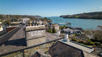 A Victorian Hotel with stone architecture, located near a body of water with boats and a pier.