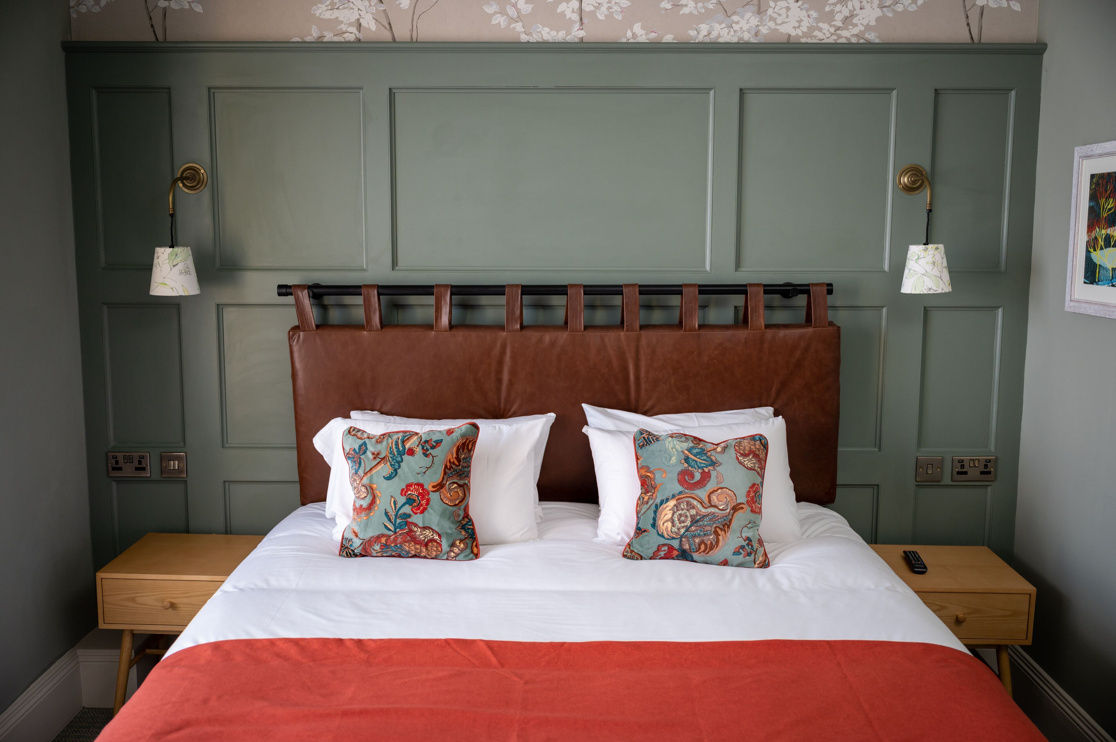 A neatly made bed with a brown headboard, two bedside lamps, and a wooden nightstand with a remote control.