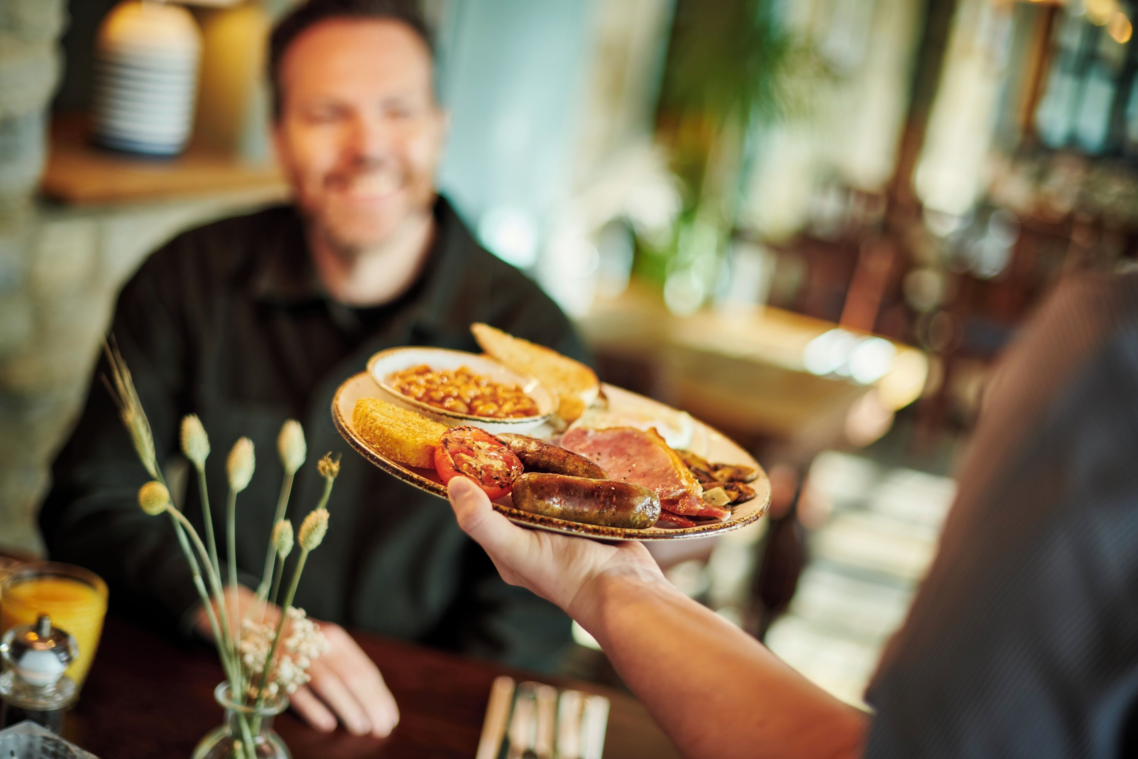 A person holding a plate with various foods, including sausages and tomatoes, in a restaurant setting.