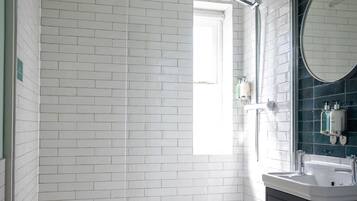 A modern bathroom with white subway tiles, a glass shower enclosure, a black vanity with a round mirror, and a toilet.