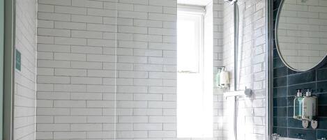 Un baño moderno con azulejos blancos tipo metro, cabina de ducha de cristal, tocador negro y espejo redondo, y un inodoro.