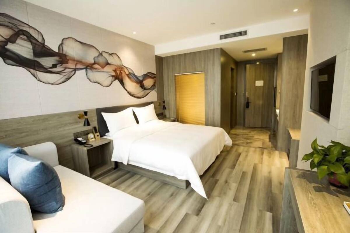 Une chambre d’hôtel moderne équipée d’un grand lit, d’un canapé, d’un bureau et d’un téléviseur fixé au mur.