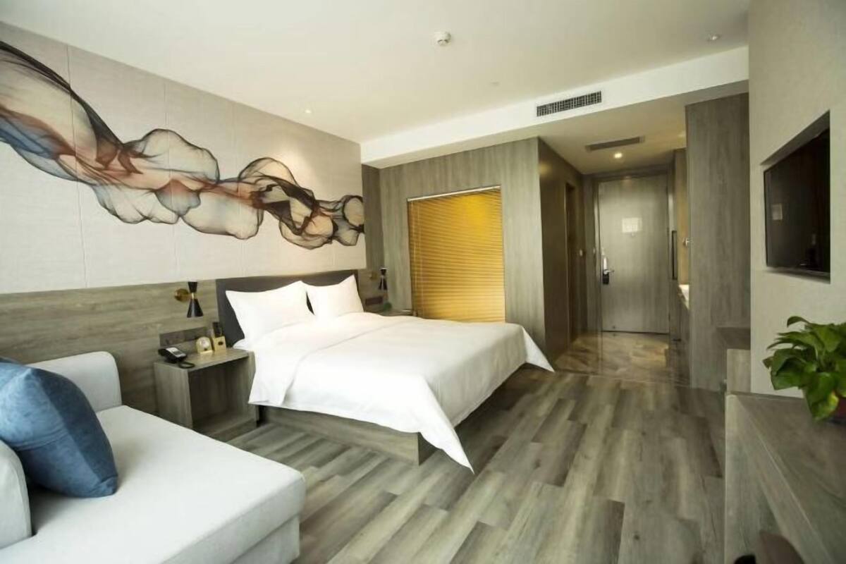 Une chambre d’hôtel moderne dotée d’un grand lit, d’un canapé, d’un téléviseur fixé au mur et d’un grand tableau abstrait.