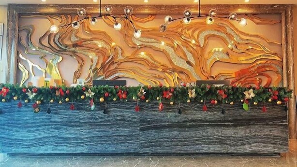 Een receptiezone met een marmeren wand, een houten receptiebalie en een bloemkrans van rode en witte bloemen.