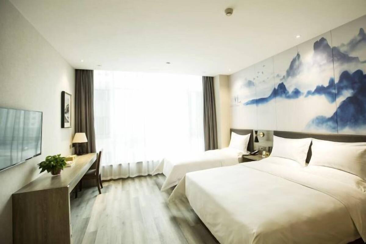 Une chambre d’hôtel avec deux lits, un bureau, une télévision et un grand tableau au mur.