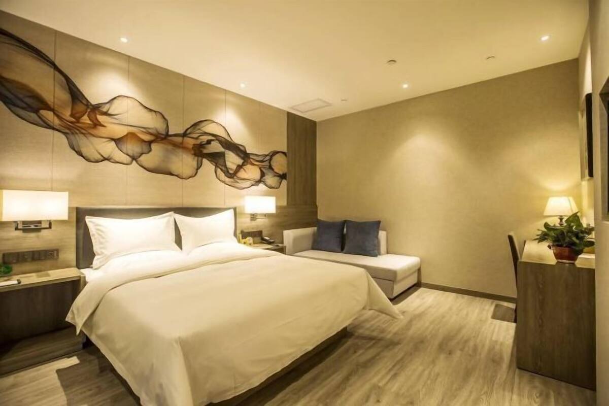 Une chambre d’hôtel moderne, dotée d’un grand lit, d’une table de chevet, d’une chaise, d’un bureau et d’une œuvre d’art accrochée au mur.
