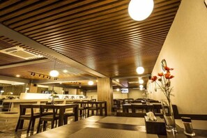 A restaurant with wooden ceiling panels, tables, chairs, and a wall-mounted TV.