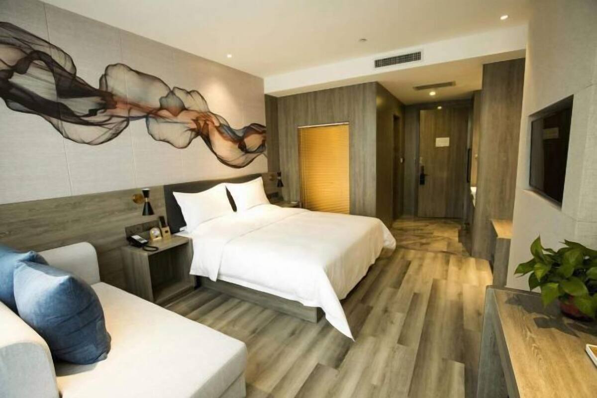 Une chambre d’hôtel moderne avec un grand lit, un canapé, une table de chevet, un téléviseur fixé au mur et un grand tableau abstrait.