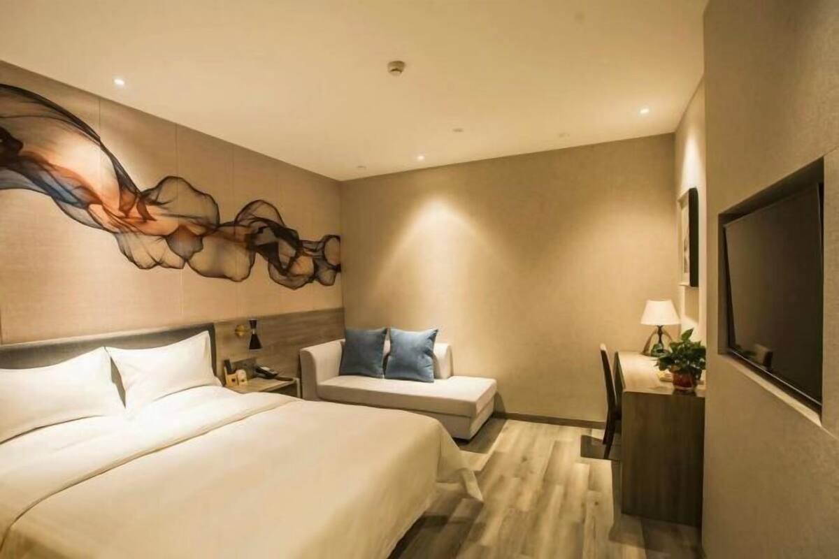 Une chambre d’hôtel comprenant un lit, un canapé, un bureau avec une lampe et un téléviseur fixé au mur.