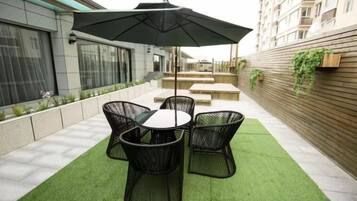 An outdoor patio with a table and chairs, an umbrella, and a wooden wall with plants.