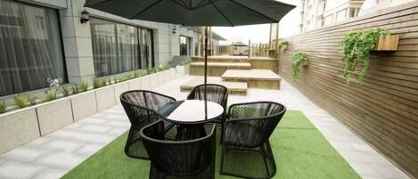 Un patio al aire libre con una mesa, sillas, una sombrilla y una pared de madera con plantas.