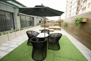 Une terrasse extérieure avec une table et des chaises, un parasol et un mur en bois orné de plantes.