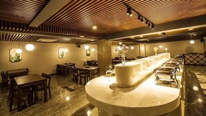 Een restaurant met een centraal marmeren aanrecht, houten plafond en ronde tafels.