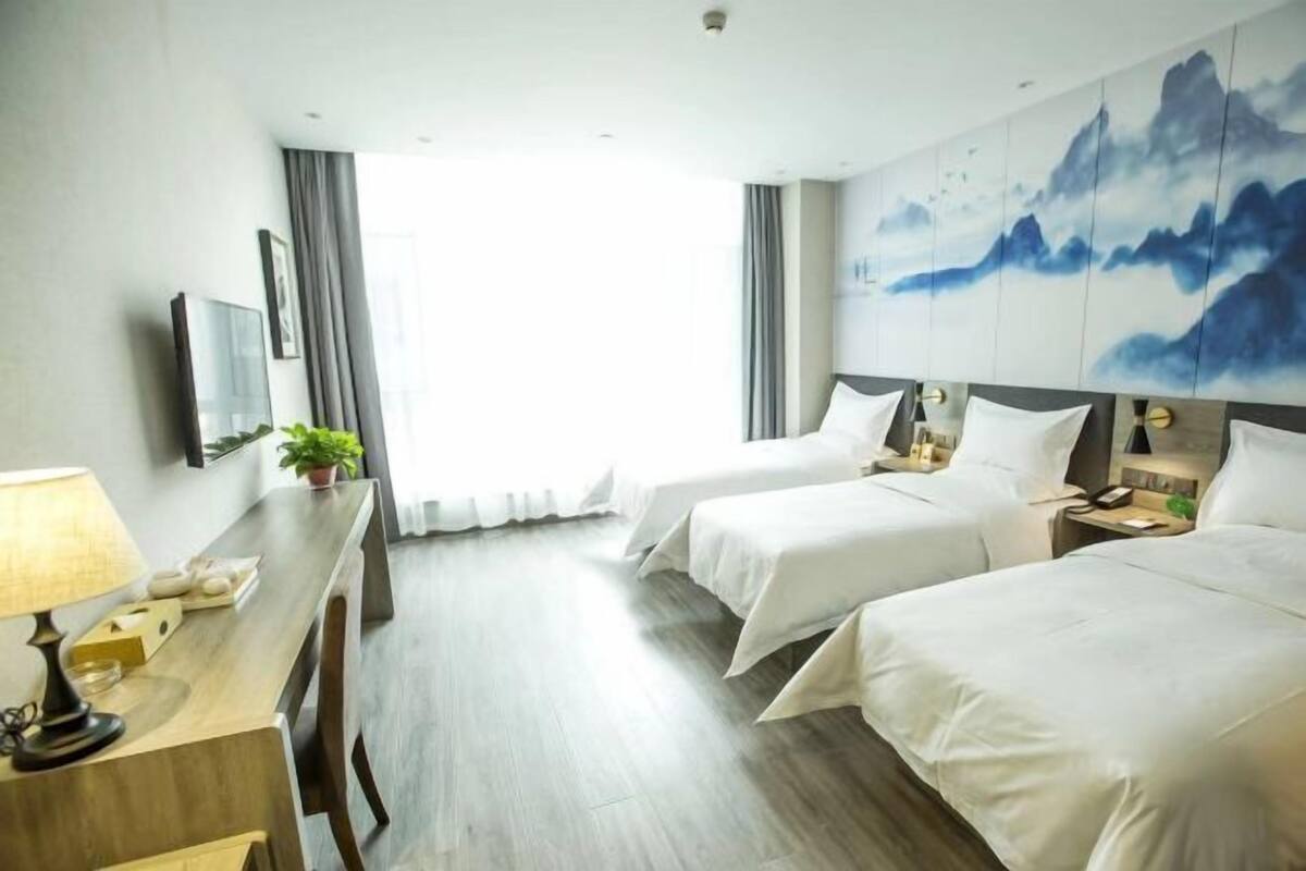 Une chambre d’hôtel avec deux lits, un bureau avec une lampe, une plante et un tableau au mur.