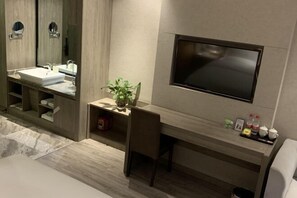 Casa de banho moderna com um espelho grande, lavatório, televisão montada na parede e um pequeno armário com produtos de higiene pessoal.