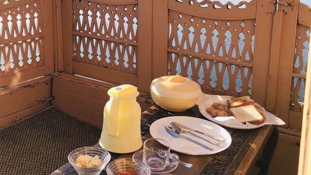 Un banco de madera con una mesa preparada para el desayuno, con vistas a un lago y montañas al fondo.