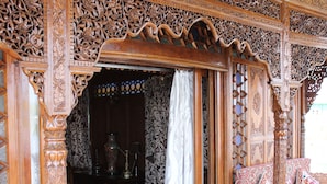 Un intrincado portón de madera que da a una habitación con un tapete estampado, una cama con cubrecama estampado y un espejo decorativo.