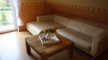 A living room with a beige leather sofa, a wooden coffee table with a vase and flowers, and a window with curtains.