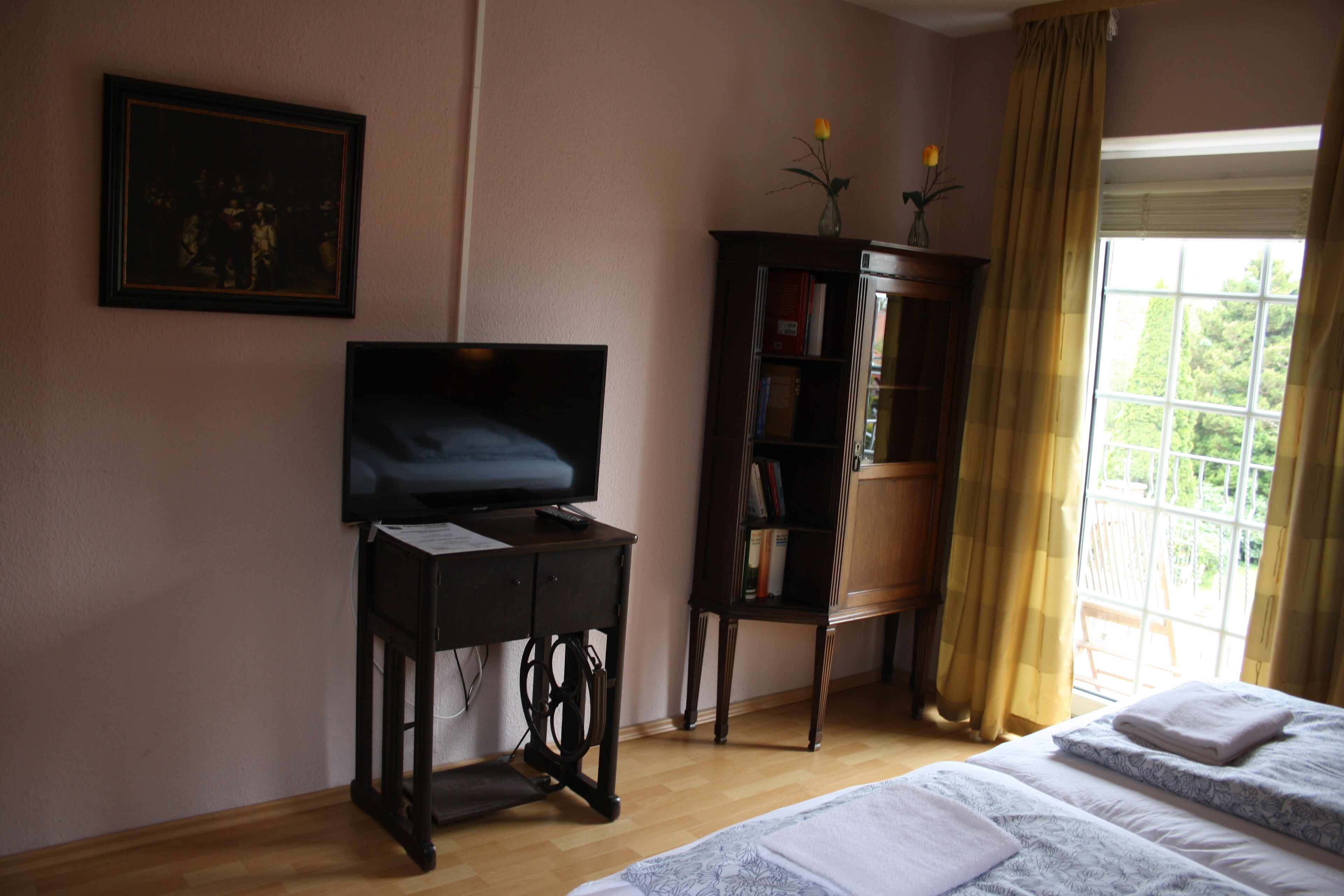 Un dormitorio con una cama, un televisor sobre un mueble de madera, una estantería y una ventana con cortinas.