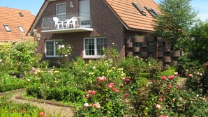 A two-story house with a brick facade, a balcony with white furniture, and a garden with various flowers. - Haus Fischernetz (Leezdorf)