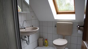 A bathroom with a sink, toilet, and a window above the toilet. - Haus Fischernetz (Leezdorf)
