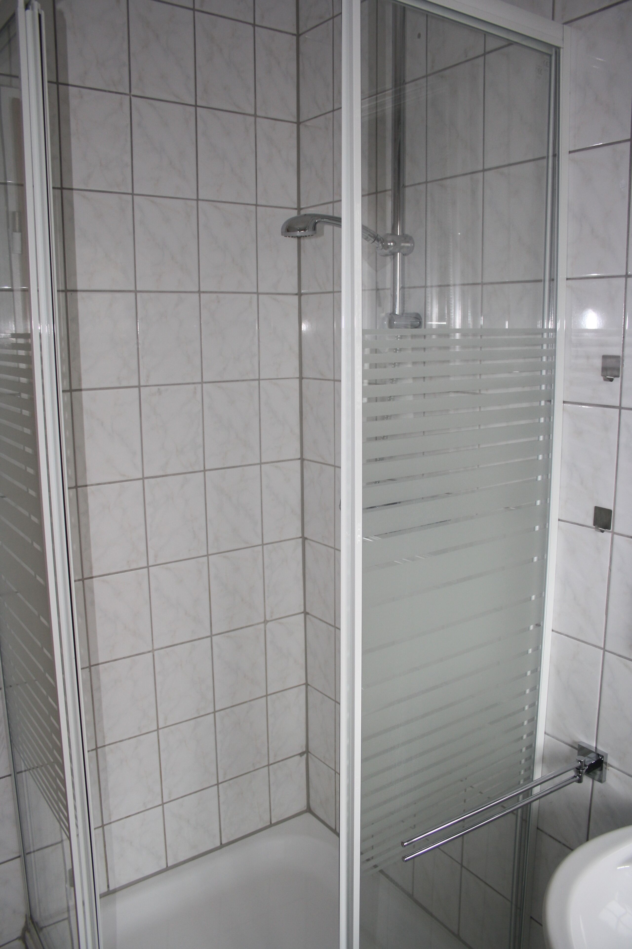A bathroom with a glass shower enclosure, white tiled walls, and a visible sink.