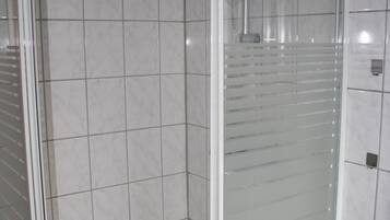 A bathroom with a glass shower enclosure, white tiled walls, and a visible sink.