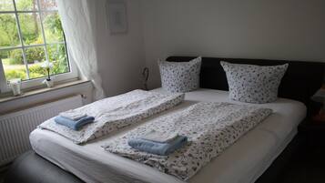 A double bed with floral bedding, two pillows, and a window with a view of greenery.