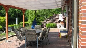 An outdoor patio with a brick floor, a covered table and chairs, and a barbecue grill. - Haus Fischernetz (Leezdorf)