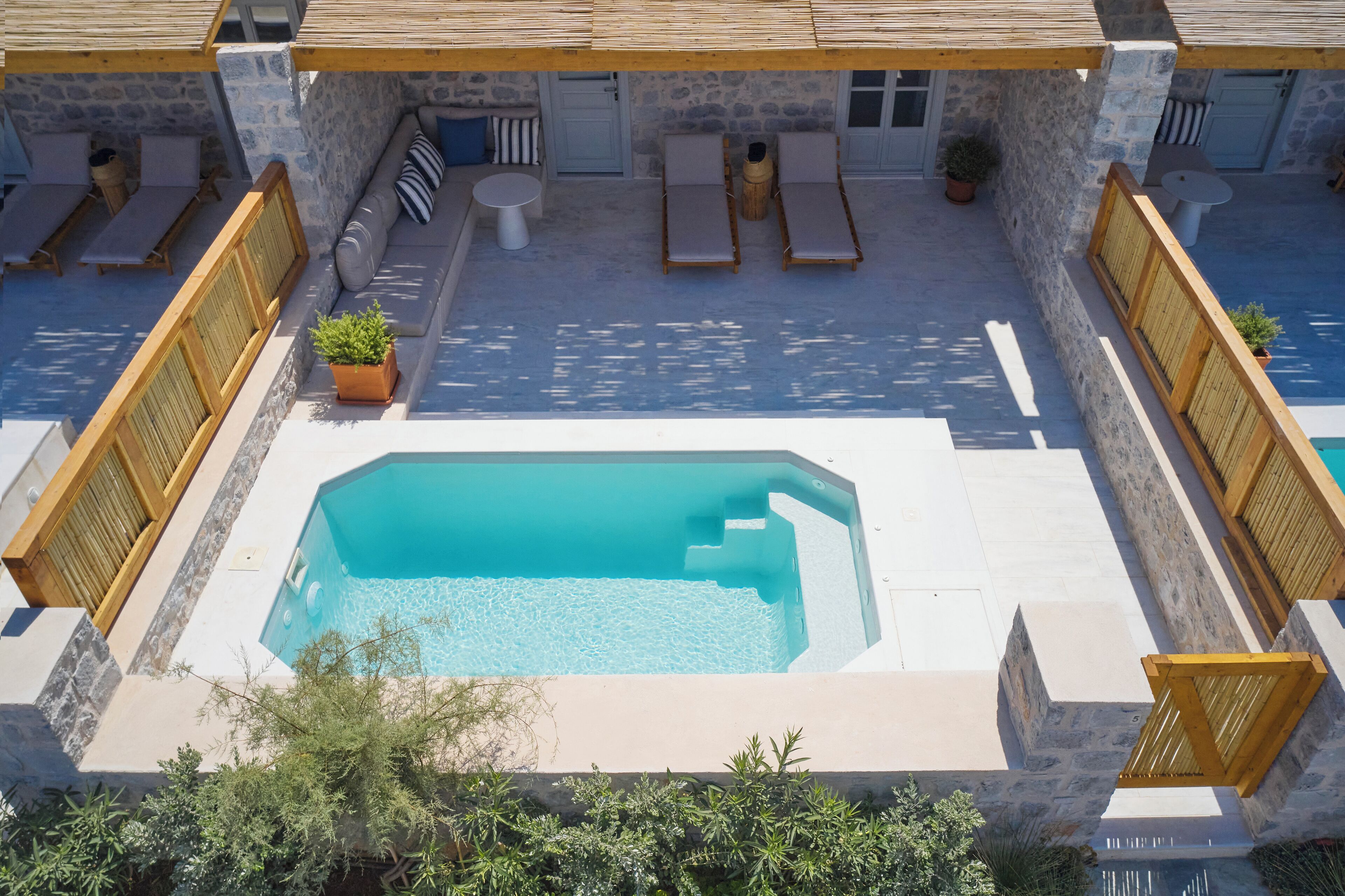Un área de piscina en la azotea con sillones de descanso y una pequeña mesa, rodeada de muros de piedra y barandas de madera.