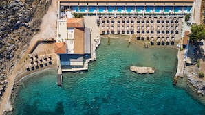 Ein Luftbild eines Küstenhotels mit Schwimmbad, Strandsonnenschirmen und einer felsigen Küstenlinie.