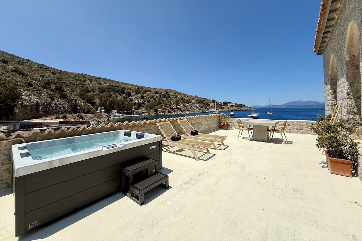 Eine Dachterrasse mit Whirlpool, Liegestühlen und Blick auf das Meer und die Hügel.