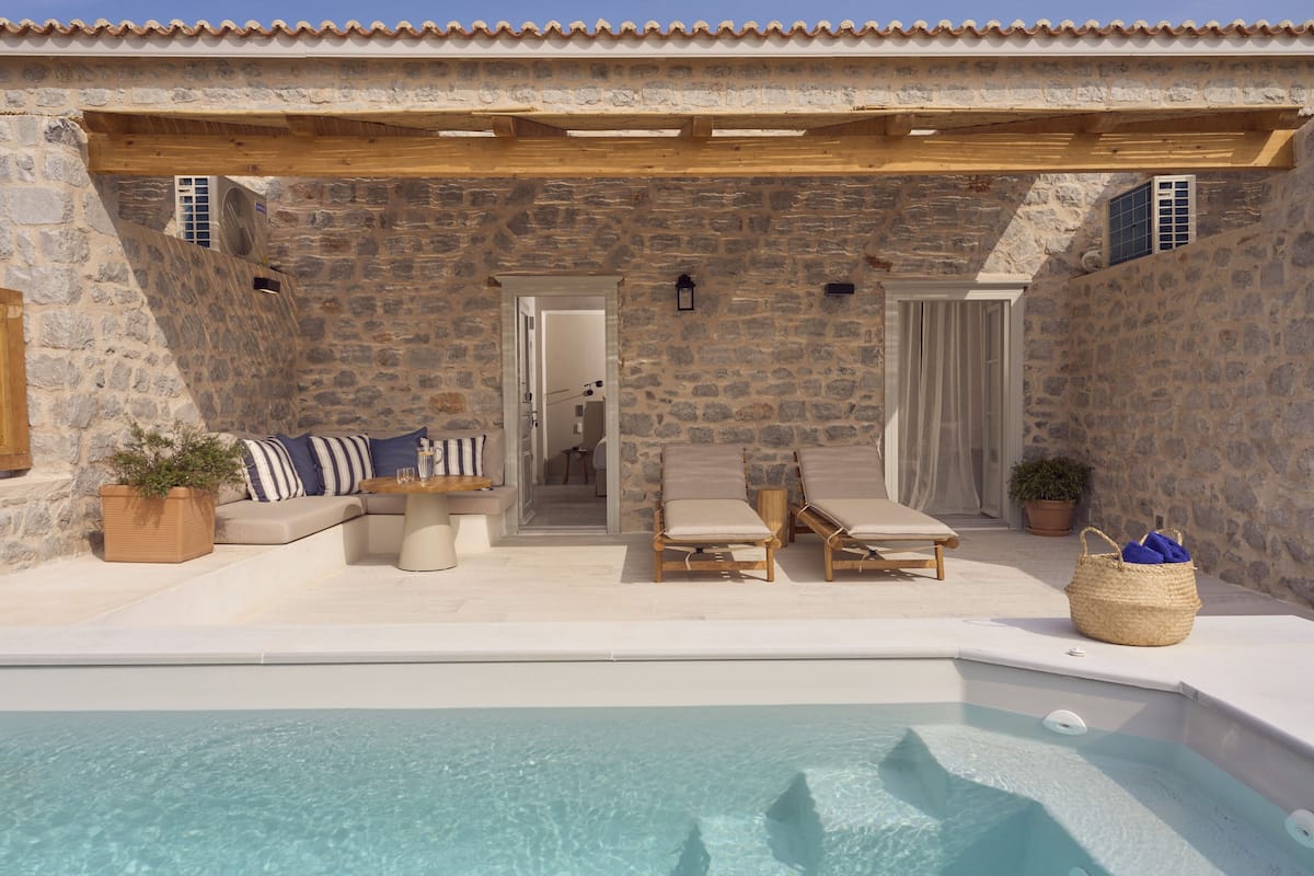 Ein Poolbereich im Freien mit Steinwänden, Liegestühlen und einer Holzpergola.
