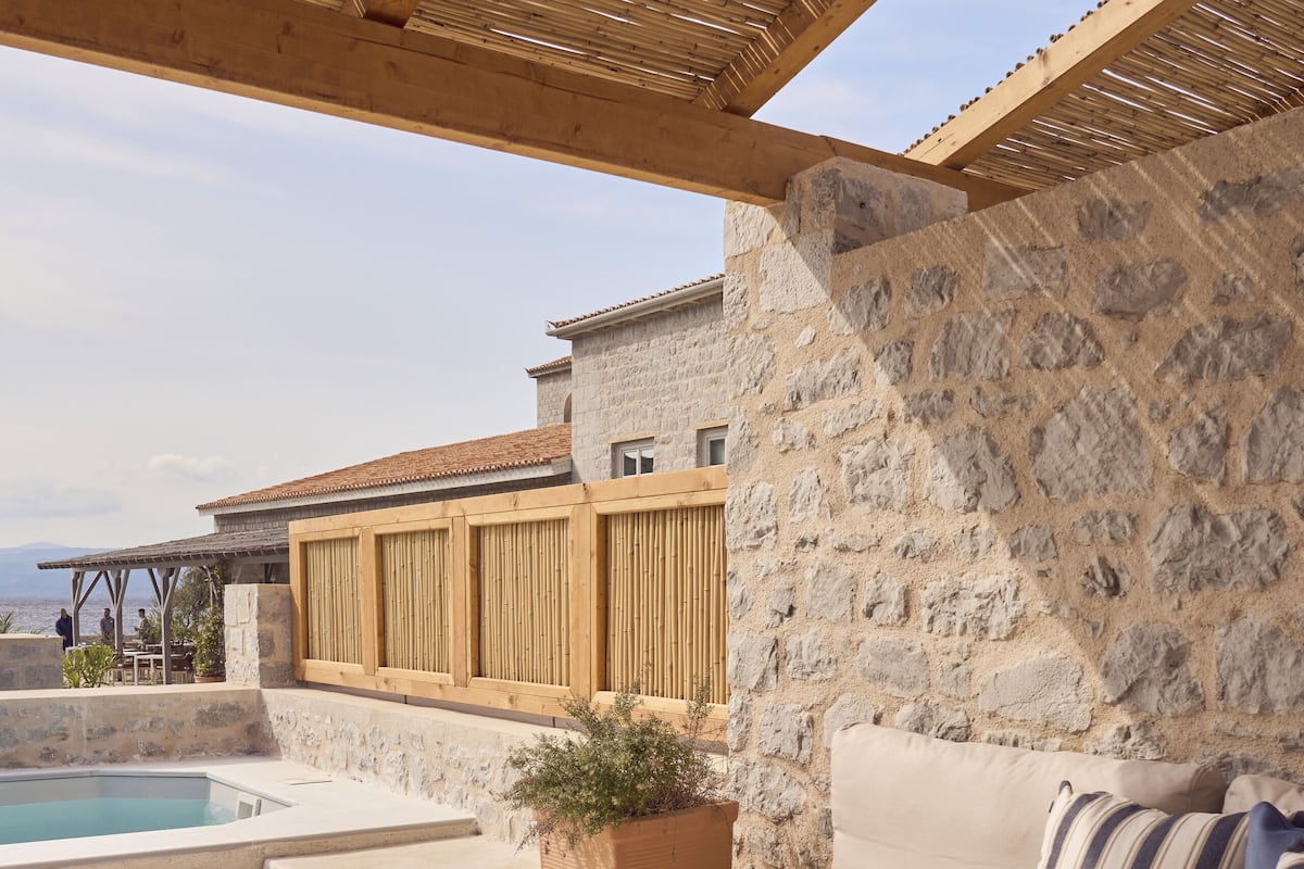 Ein Sitzbereich im Freien mit Steinmauern, einem Pool, einer Holzpergola und Blick auf das Meer.