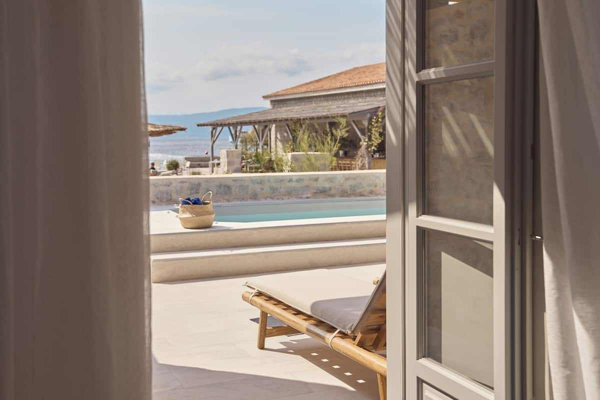 Blick auf einen Pool mit Liegestuhl, eine Steinmauer und ein Gebäude mit einem Ziegeldach im Hintergrund.