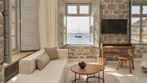 Ein gemütliches Wohnzimmer mit Steinwand, einem großen Fenster mit Meerblick, einer Couch, einem Couchtisch und einem an der Wand befestigten Fernseher.