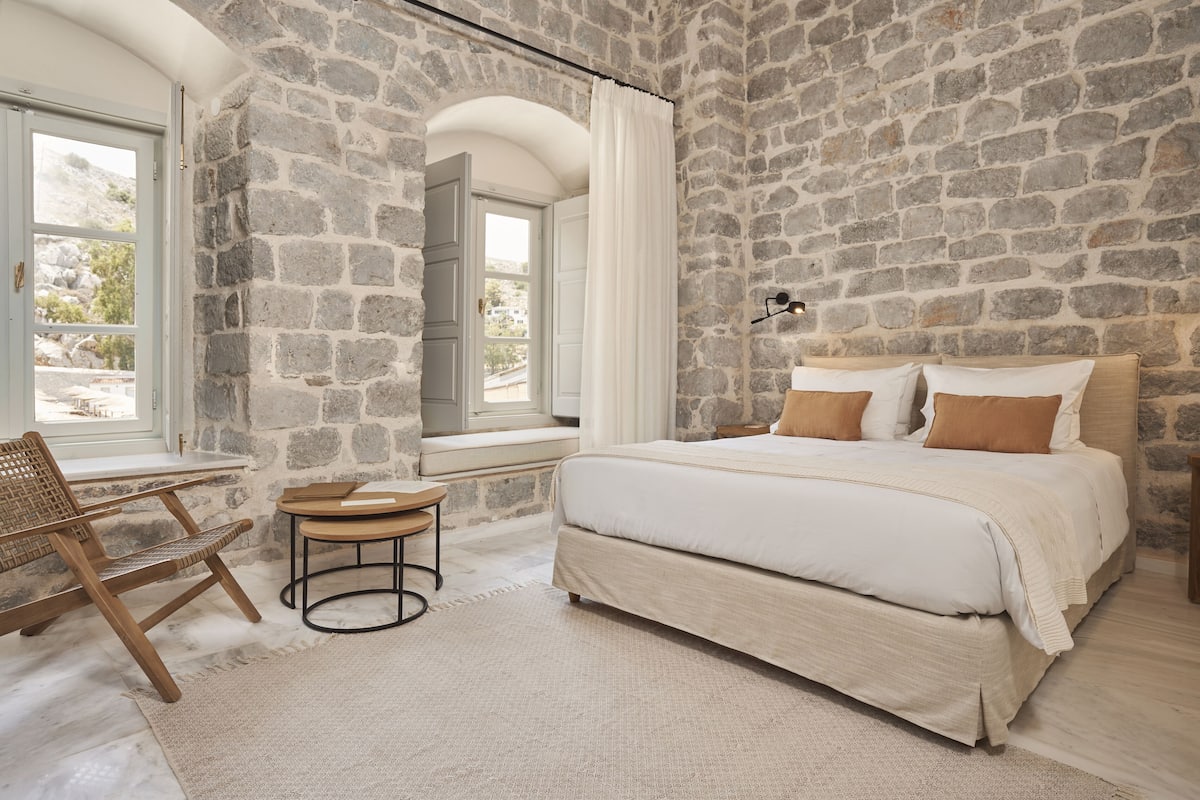 Ein Schlafzimmer mit einer Steinsandsteinwand, einem Bett mit weißer Bettwäsche, einem Holzstuhl und einem kleinen Tisch.