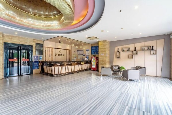 Un hall d’hôtel moderne comprenant un comptoir d’accueil, un espace salon et un grand luminaire circulaire au plafond.