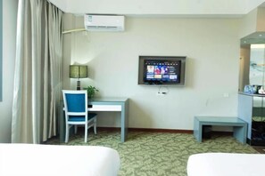 Een hotelkamer met een bed, een bureau met stoel, een aan de muur bevestigde televisie en een airconditioning.