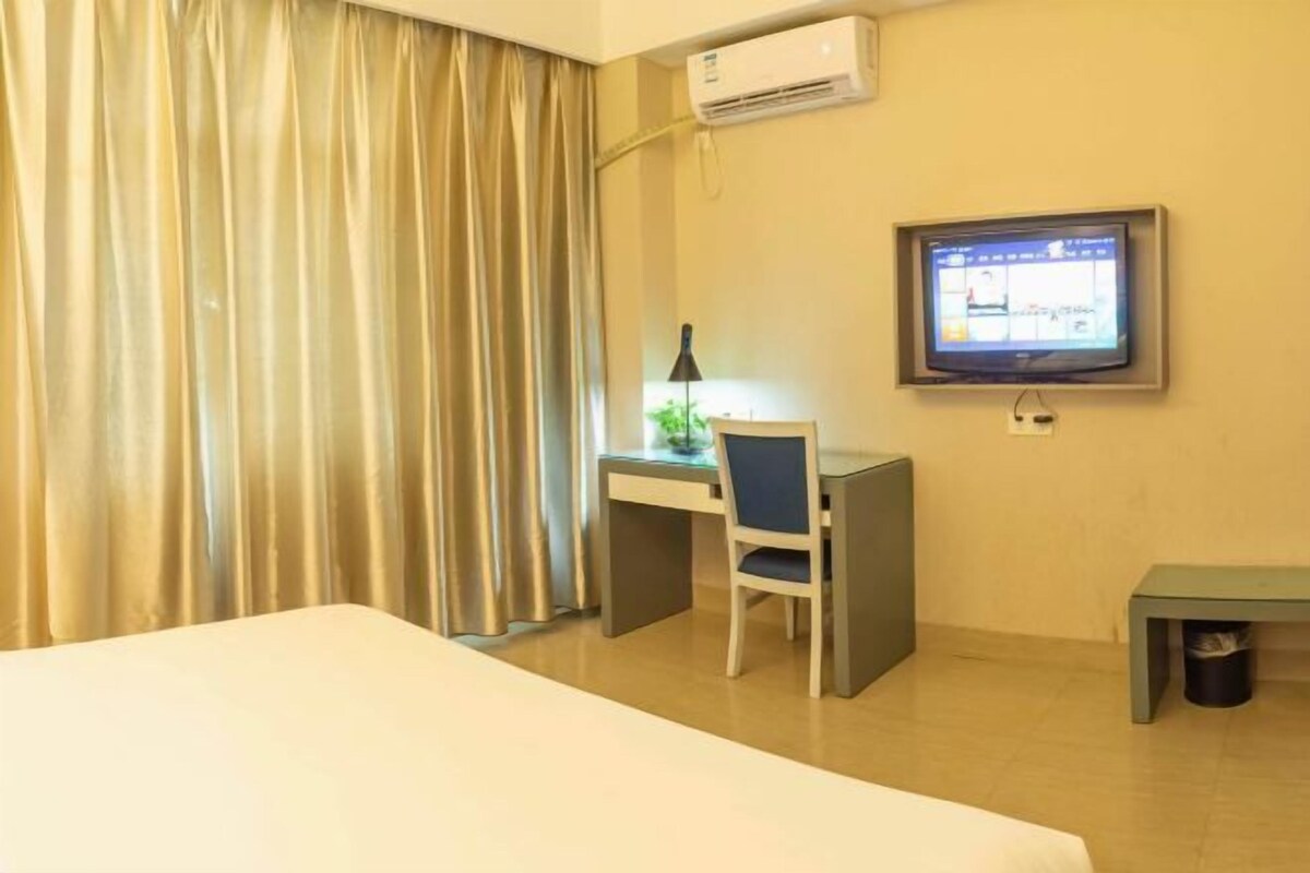 Een hotelkamer met een bed, een bureau met een stoel, een televisie en een airconditioning.