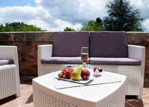 Un área de estar al aire libre con mimbre, una mesa con fruta y una copa de vino.