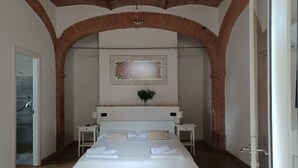 Une chambre à coucher avec un grand lit, une table de chevet, une lampe fixée au mur et une porte donnant sur une salle de bain.