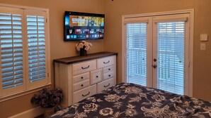 Un dormitorio con televisor montado en la pared, cómoda, cama con colcha floral y candelabro.