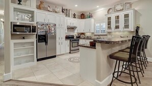 Una cocina moderna con armarios blancos, electrodomésticos de acero inoxidable y una isla central con taburetes de bar.