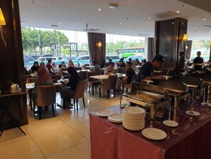 A buffet-style restaurant with multiple dining tables and chairs, a buffet counter with food trays, and a view of parked cars outside. - Le'venue Hotel (Kajang)